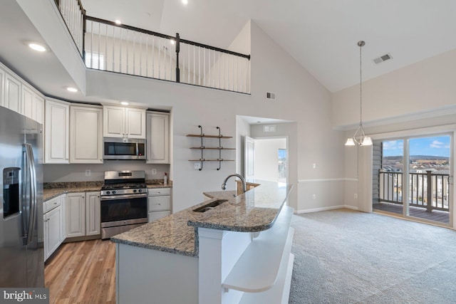 kitchen featuring stainless steel appliances, light stone countertops, decorative light fixtures, sink, and white cabinetry