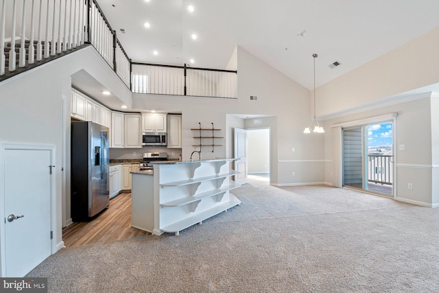 kitchen with a high ceiling, hanging light fixtures, stainless steel appliances, white cabinets, and light carpet