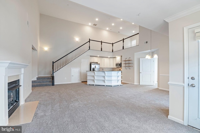 unfurnished living room featuring ornamental molding, light carpet, and a high ceiling