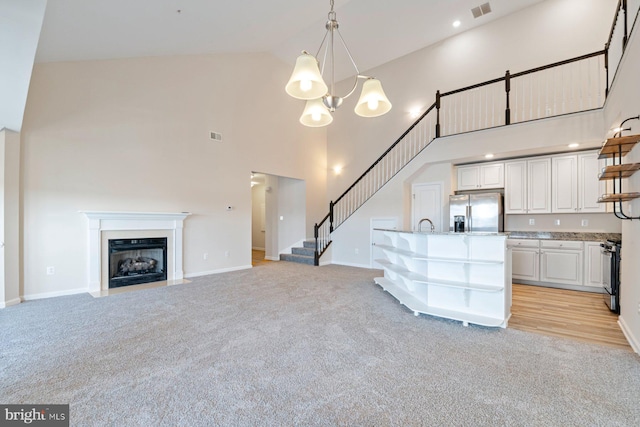 unfurnished living room with high vaulted ceiling, an inviting chandelier, and light colored carpet