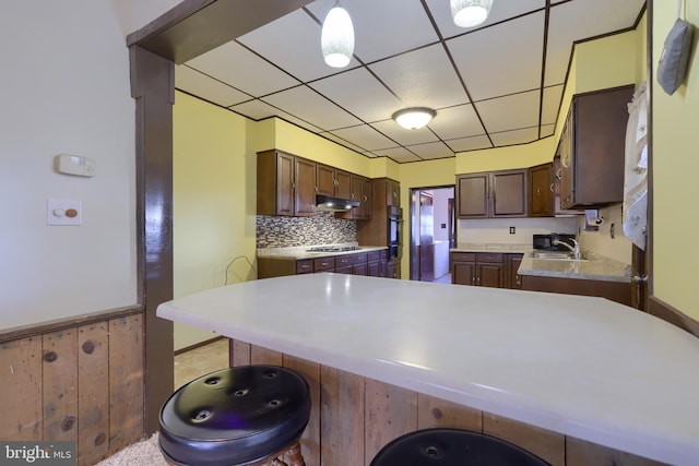 kitchen with a breakfast bar, sink, hanging light fixtures, kitchen peninsula, and a drop ceiling