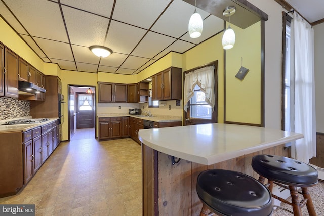 kitchen with a paneled ceiling, pendant lighting, stainless steel gas stovetop, tasteful backsplash, and a kitchen breakfast bar