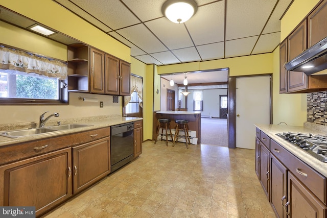 kitchen featuring a paneled ceiling, tasteful backsplash, black dishwasher, sink, and stainless steel gas cooktop