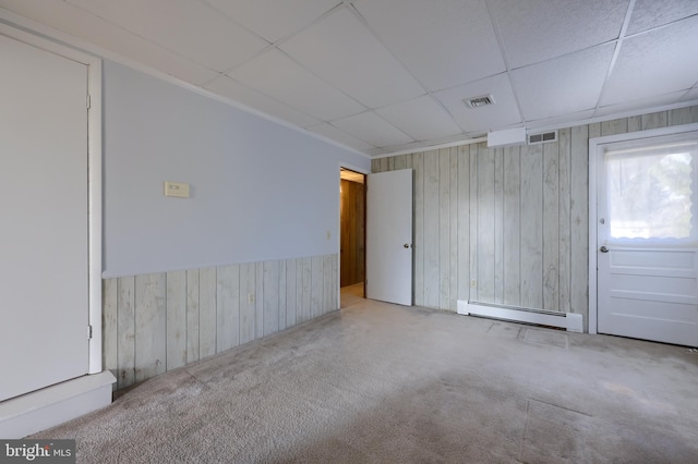 carpeted spare room featuring a baseboard heating unit, a drop ceiling, and wood walls