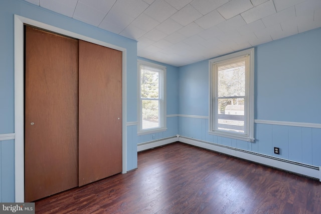 unfurnished bedroom with dark wood-type flooring, baseboard heating, and a closet