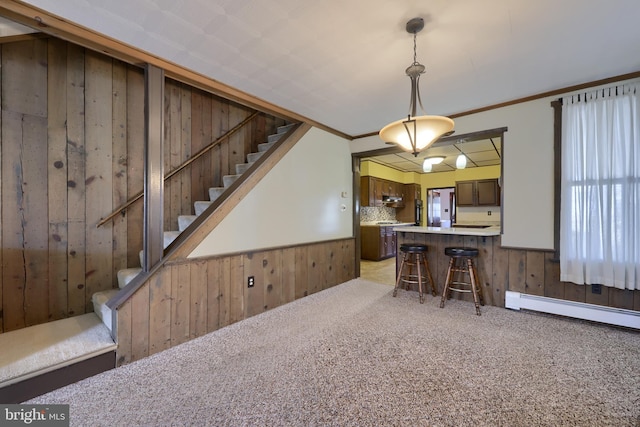 kitchen with crown molding, a breakfast bar, hanging light fixtures, light carpet, and wood walls