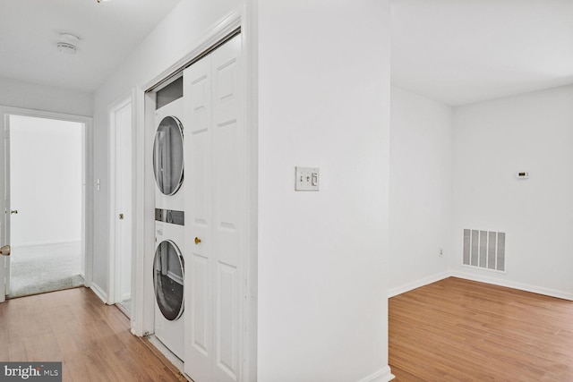 clothes washing area featuring stacked washer and dryer and light wood-type flooring