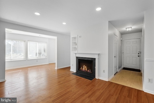 unfurnished living room with light wood-type flooring, a fireplace, and built in features