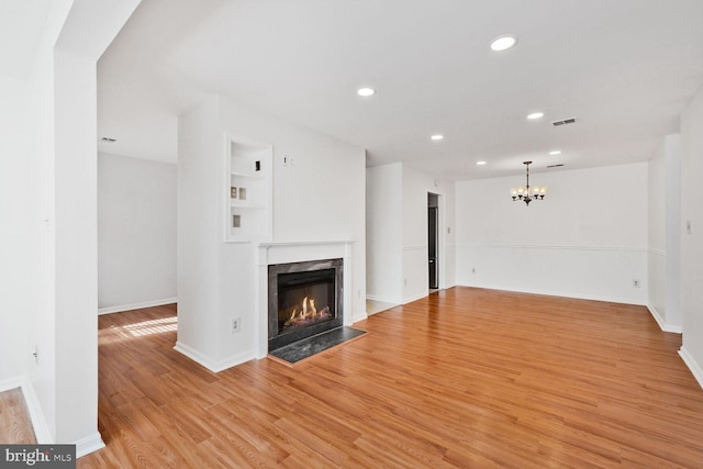 unfurnished living room with light wood-type flooring, an inviting chandelier, and a high end fireplace