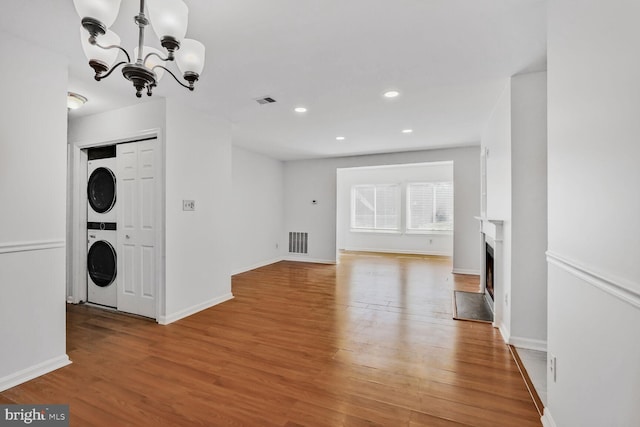 unfurnished living room with stacked washer and dryer, a chandelier, and light hardwood / wood-style floors