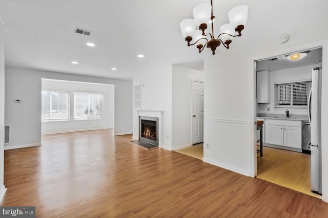 unfurnished living room with a notable chandelier, sink, and light wood-type flooring