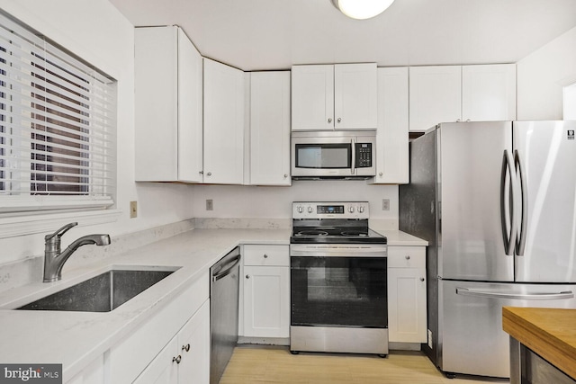 kitchen with appliances with stainless steel finishes, sink, light stone counters, light hardwood / wood-style floors, and white cabinets