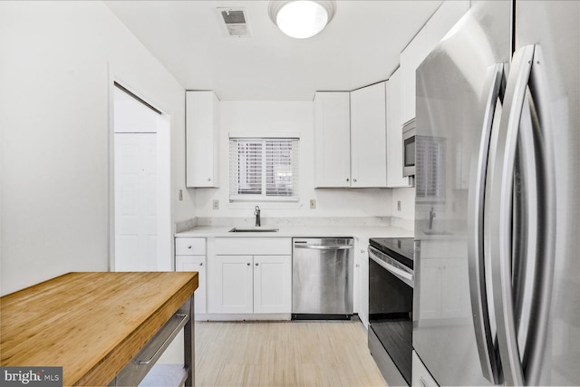 kitchen featuring white cabinetry, sink, stainless steel appliances, and light wood-type flooring