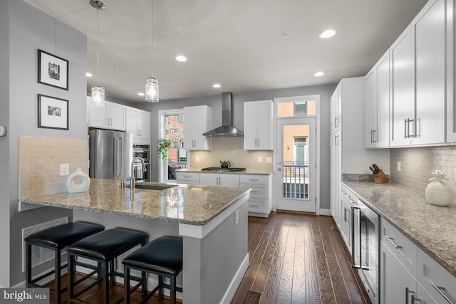 kitchen featuring dark wood-type flooring, a breakfast bar, stainless steel appliances, a peninsula, and wall chimney exhaust hood