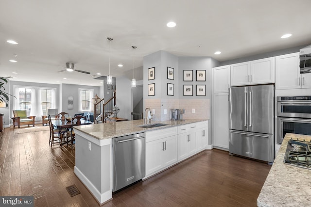 kitchen with a sink, dark wood-style floors, stainless steel appliances, a peninsula, and white cabinets