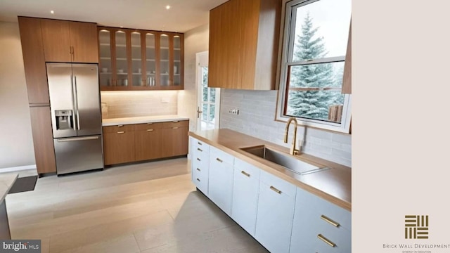 kitchen with stainless steel refrigerator with ice dispenser, plenty of natural light, sink, and white cabinets