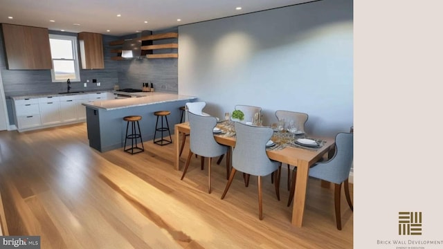 kitchen with white cabinetry, sink, backsplash, wall chimney range hood, and light wood-type flooring