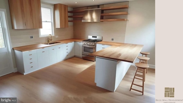 kitchen featuring stainless steel range with gas cooktop, range hood, white cabinetry, butcher block counters, and sink