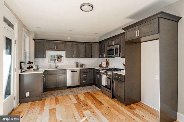 kitchen featuring sink, backsplash, stainless steel appliances, dark brown cabinets, and light wood-type flooring