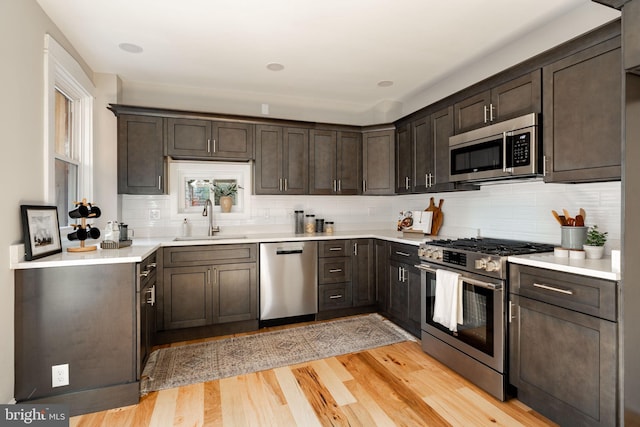 kitchen with dark brown cabinetry, sink, light hardwood / wood-style flooring, appliances with stainless steel finishes, and backsplash