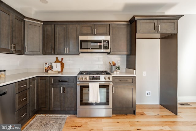 kitchen with dark brown cabinetry, backsplash, light wood-type flooring, and appliances with stainless steel finishes