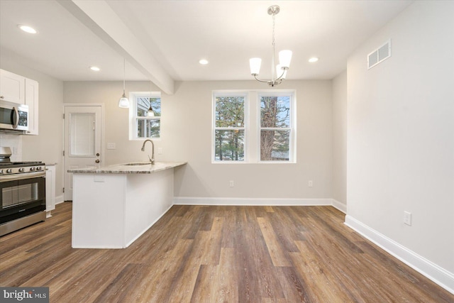 kitchen with appliances with stainless steel finishes, hanging light fixtures, light stone countertops, white cabinets, and kitchen peninsula