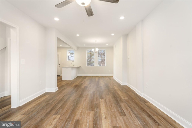 spare room with ceiling fan with notable chandelier, dark wood-type flooring, and sink