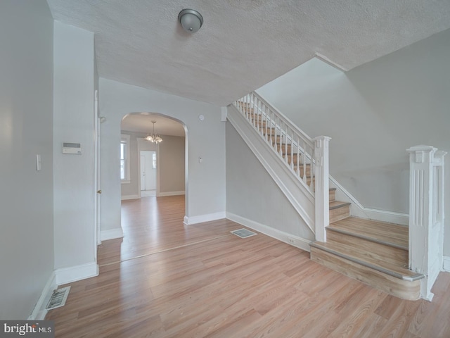 empty room with arched walkways, visible vents, stairway, and wood finished floors