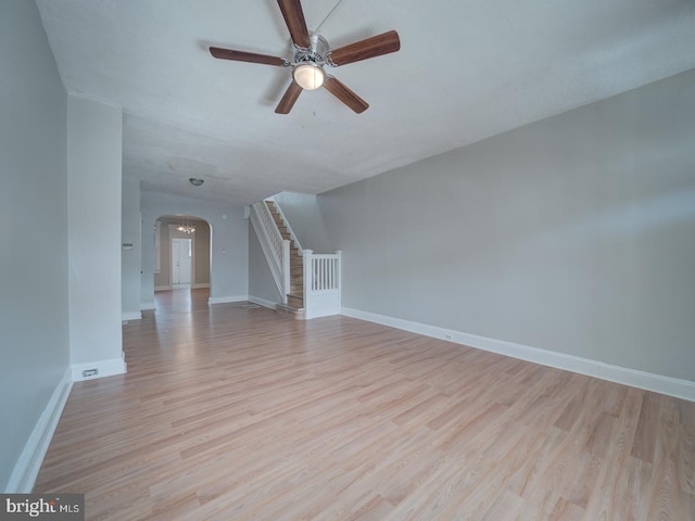 unfurnished living room with light wood-type flooring, arched walkways, stairway, and baseboards