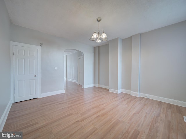 spare room featuring a chandelier, arched walkways, light wood-style flooring, and baseboards