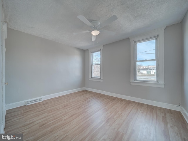 empty room featuring a textured ceiling, wood finished floors, visible vents, and baseboards