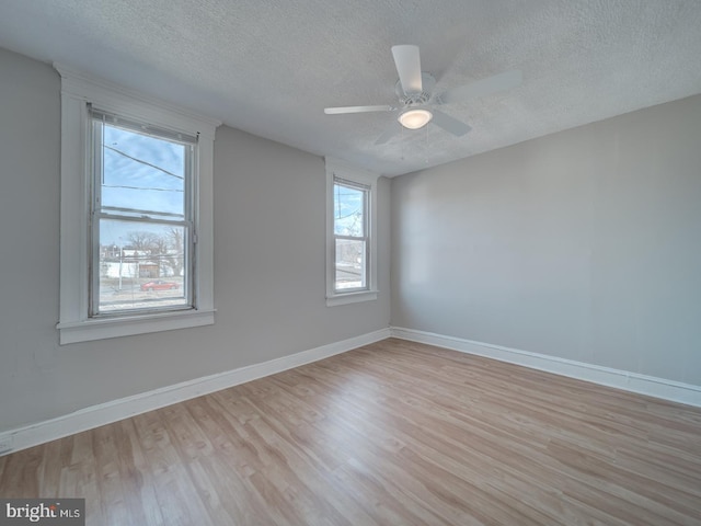 unfurnished room with light wood-type flooring, a textured ceiling, and baseboards