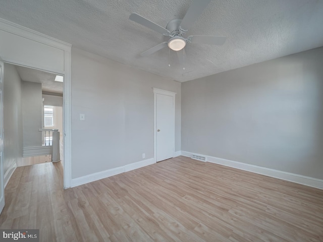 unfurnished room featuring a textured ceiling, light wood finished floors, visible vents, and baseboards