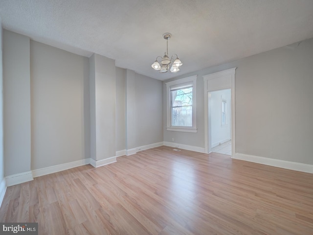 unfurnished room with baseboards, a textured ceiling, light wood-style flooring, and an inviting chandelier