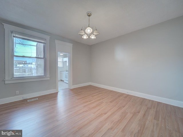 unfurnished room featuring baseboards, light wood-style floors, visible vents, and a notable chandelier