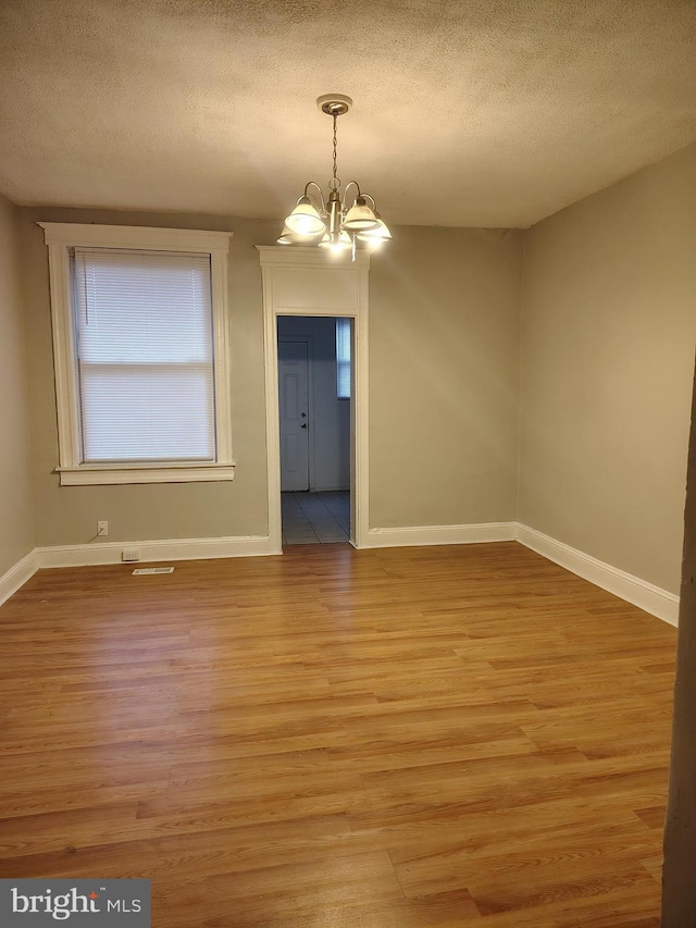 unfurnished dining area featuring light wood finished floors, a notable chandelier, and a textured ceiling