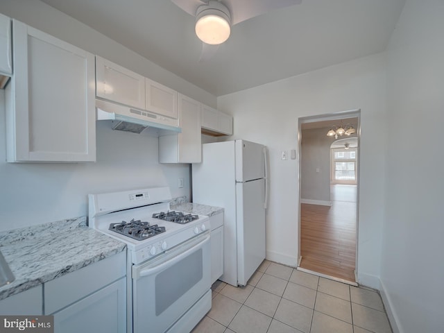 kitchen with light tile patterned flooring, under cabinet range hood, white appliances, white cabinetry, and baseboards