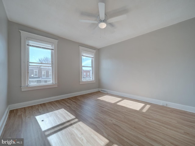 spare room with visible vents, wood finished floors, a ceiling fan, and baseboards