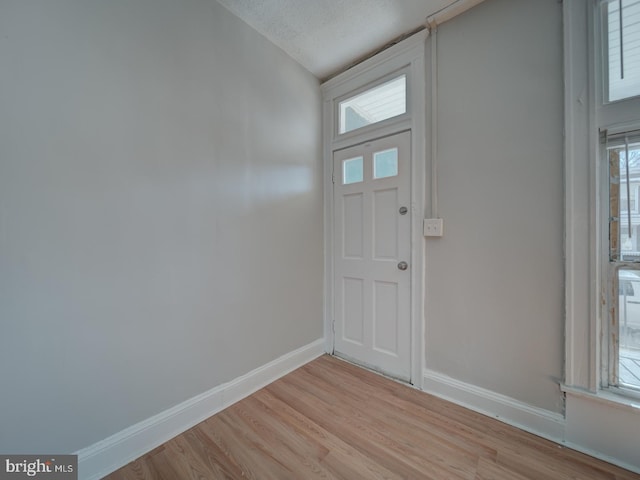 entryway with a textured ceiling, light wood-type flooring, and baseboards