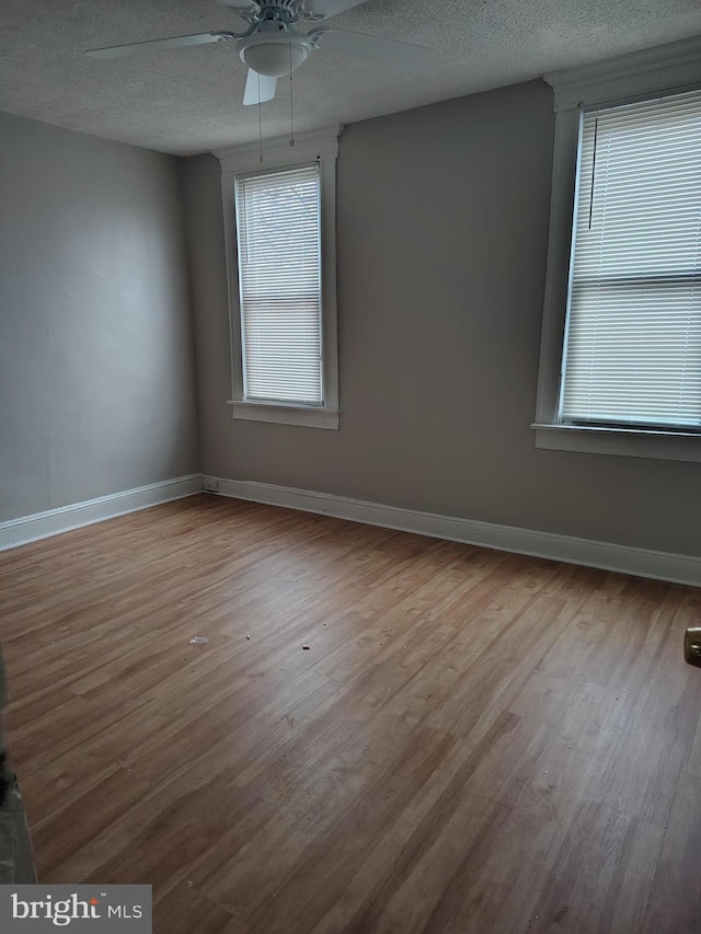 unfurnished room with a textured ceiling, wood finished floors, and baseboards