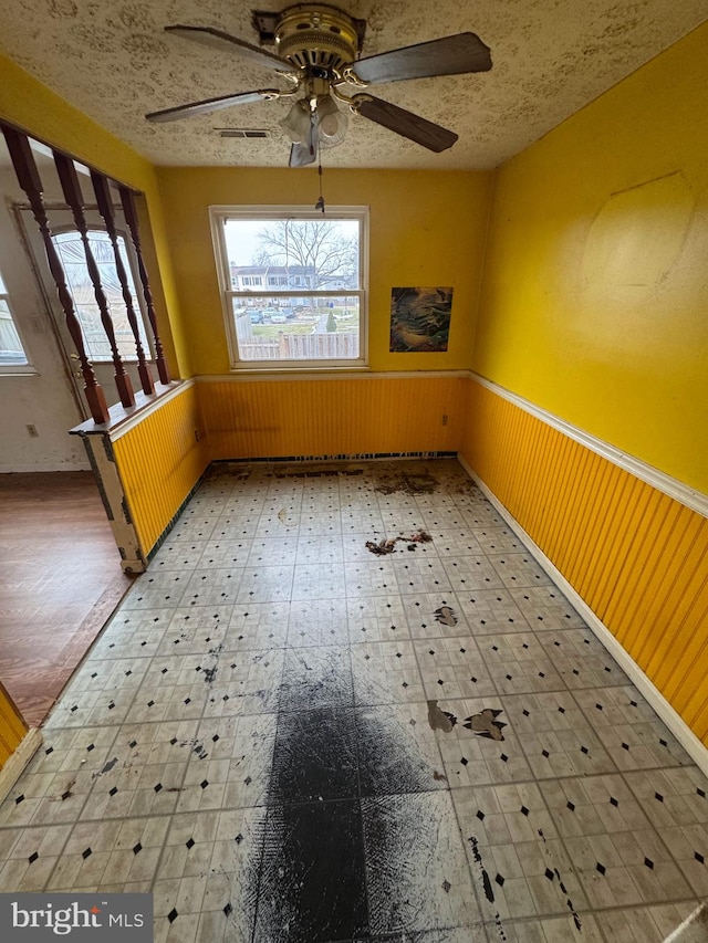 unfurnished dining area with ceiling fan, wooden walls, and a textured ceiling