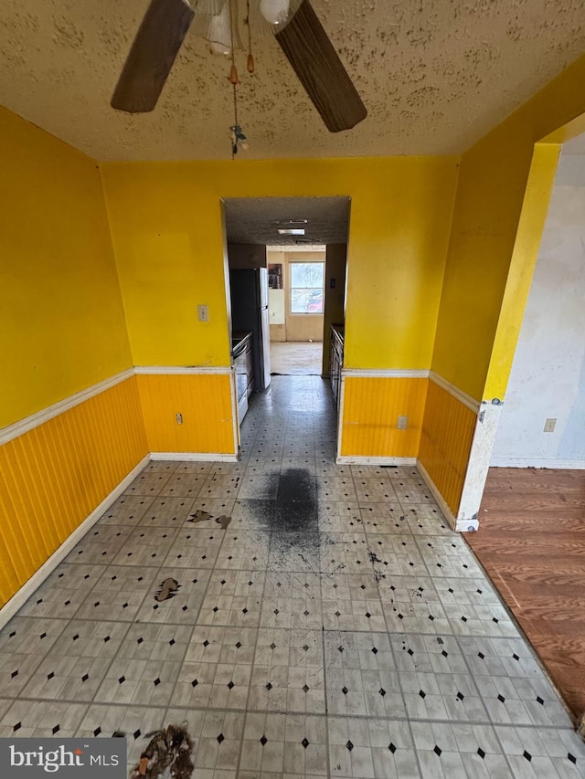 spare room with a textured ceiling, wooden walls, and ceiling fan