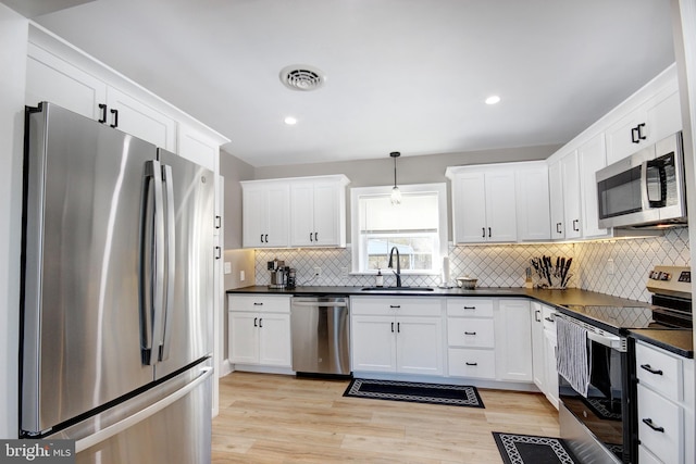 kitchen featuring appliances with stainless steel finishes, pendant lighting, sink, white cabinets, and light hardwood / wood-style floors