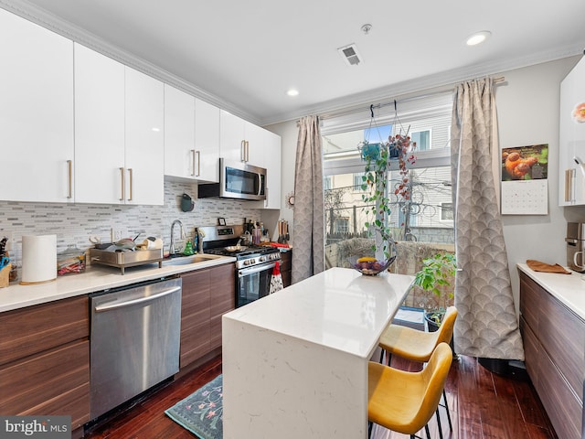 kitchen with a breakfast bar, dark hardwood / wood-style floors, white cabinetry, decorative backsplash, and stainless steel appliances