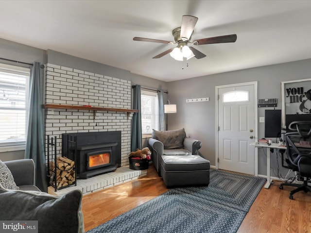 living area with a brick fireplace, ceiling fan, and wood finished floors