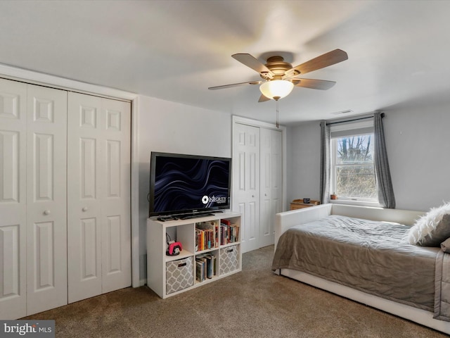 carpeted bedroom featuring ceiling fan, visible vents, and two closets