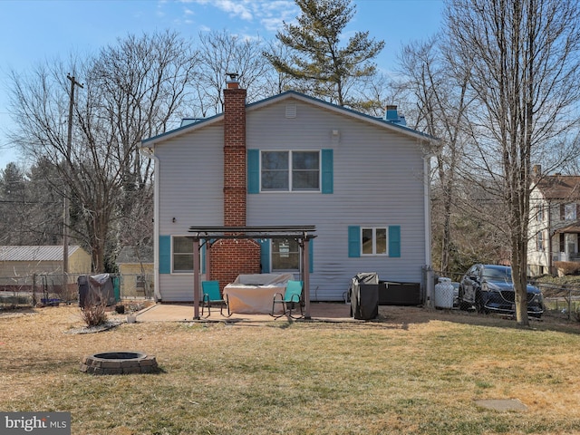 back of house featuring an outdoor fire pit, a chimney, fence, and a lawn