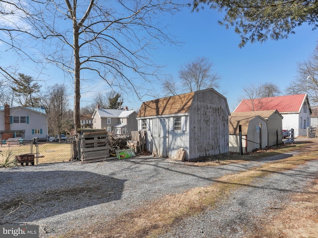 view of shed with a residential view, gravel driveway, and fence