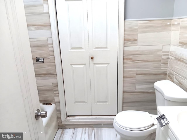 bathroom featuring vanity, toilet, and tile walls