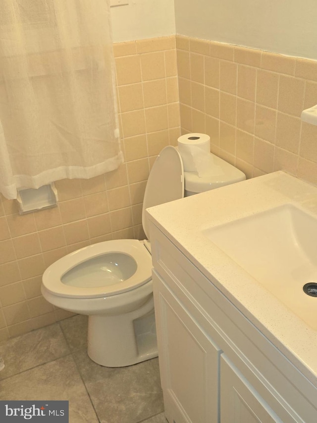 half bathroom featuring tile patterned floors, tile walls, toilet, and vanity